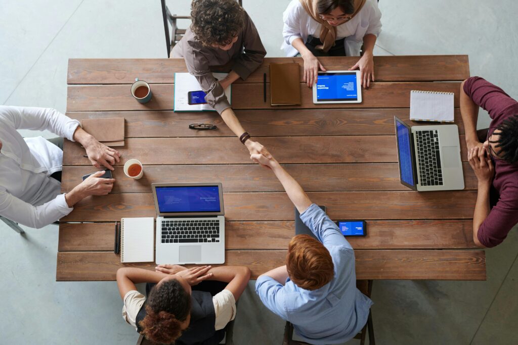 Geçerli görsel: Overhead view of colleagues in a work meeting using laptops and tablets, emphasizing teamwork and technology.